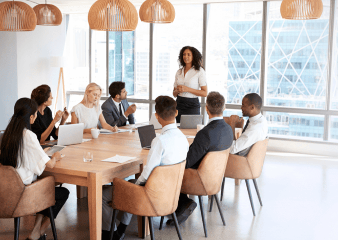 Businesswoman leading a meeting with a diverse team in a modern office with large windows.