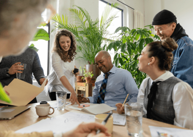 Colleagues sharing a laugh during a collaborative meeting in a plant-filled office.