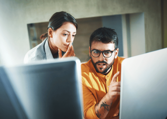 Two colleagues analyzing data on computer screens.