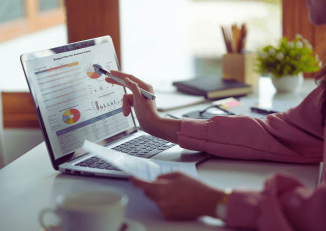 Person pointing at data charts on a laptop during a meeting.