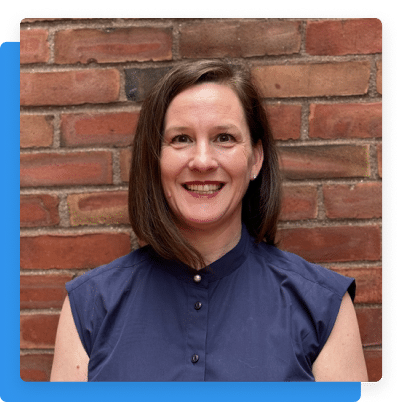 Portrait of a smiling woman, Monique McDonough, standing in front of a brick wall.