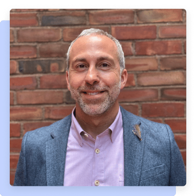 Portrait of a smiling man, Rob Catalano, standing in front of a brick wall.