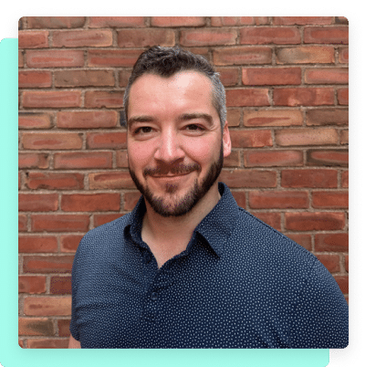 Portrait of a smiling man, Stephen Shinnan, standing in front of a brick wall.