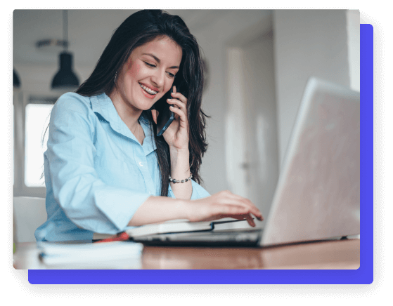 Woman smiling while working on a laptop and talking on the phone.