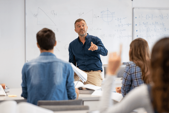 Teacher at front of class in front of a whiteboard.