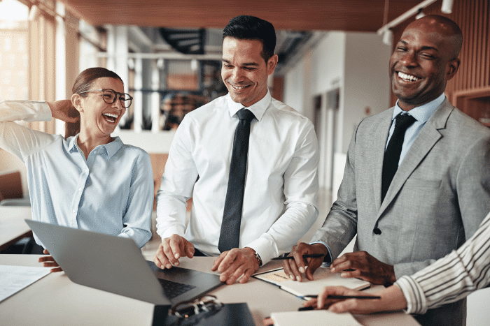 Three people standing around a table with a laptop on it.