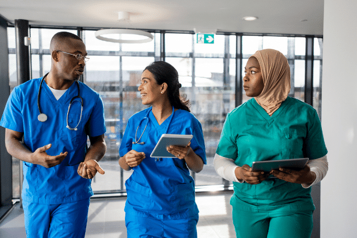 Three people in medical scrubs walking and talking.