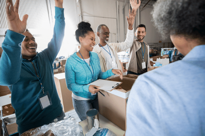 Group of people filling boxes, celebrating with their hands raised.