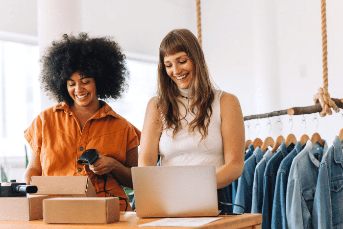 Two women standing at a counter, one is scanning a label on a box and the other is typing on a computer.