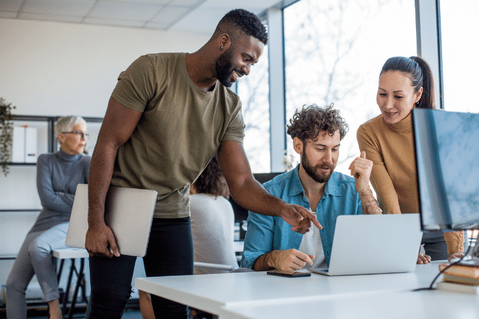 Group of people standing around a computer, pointing and talking.