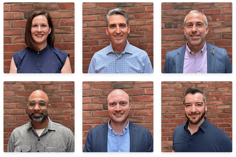 Group portrait of WorkTango's leadership team standing against a brick wall background.