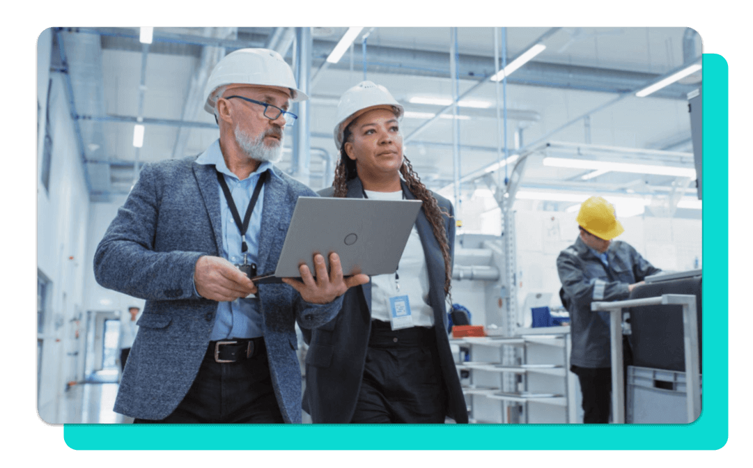 Two people in white hard hats walking a manufacturing plant floor.