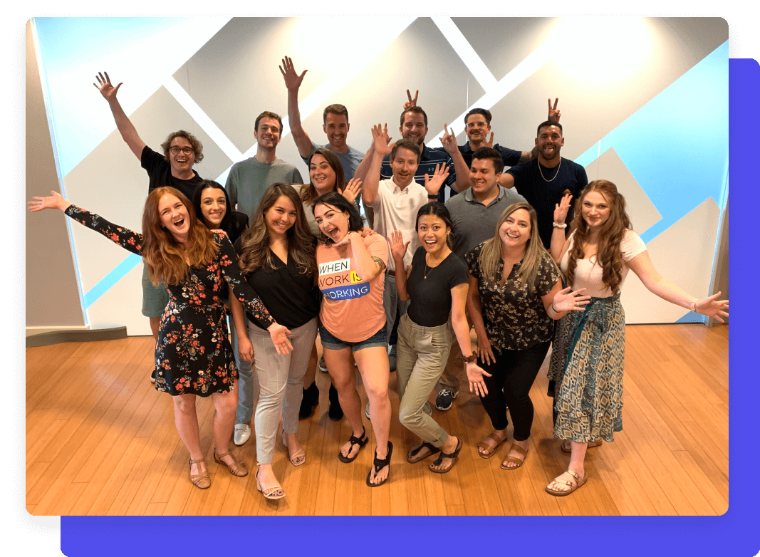 Group photo of a cheerful team posing with playful gestures against a geometric-patterned wall.