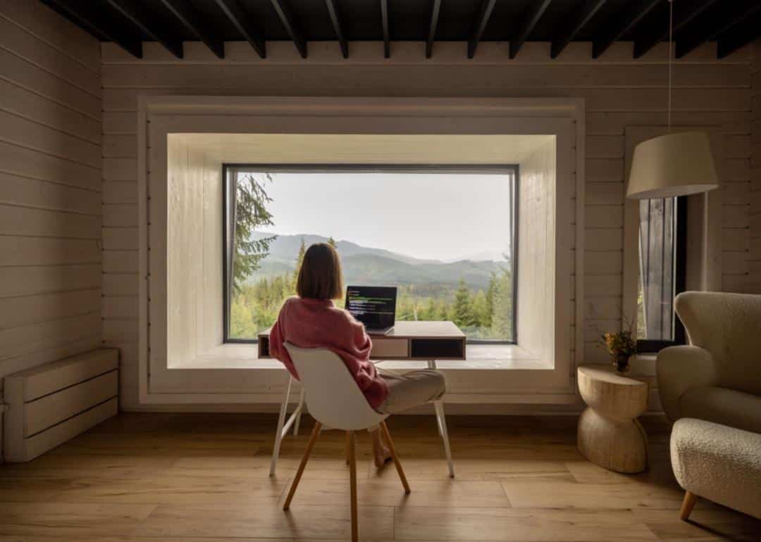 Sitting at a desk with a computer, staring out the window at a mountainous landscape.